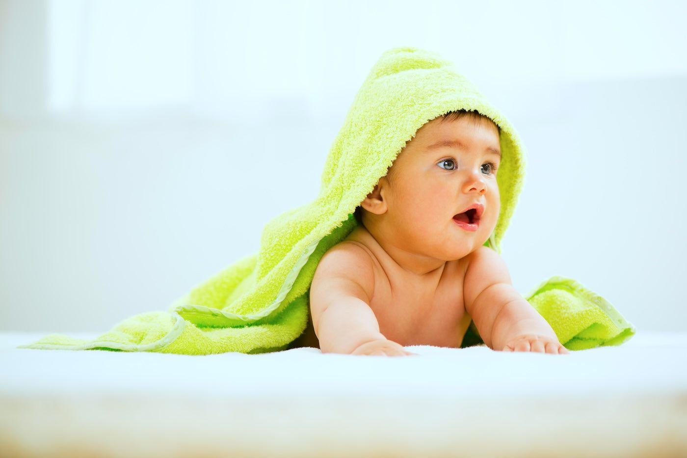 Baby on belly wearing bright green hooded towel