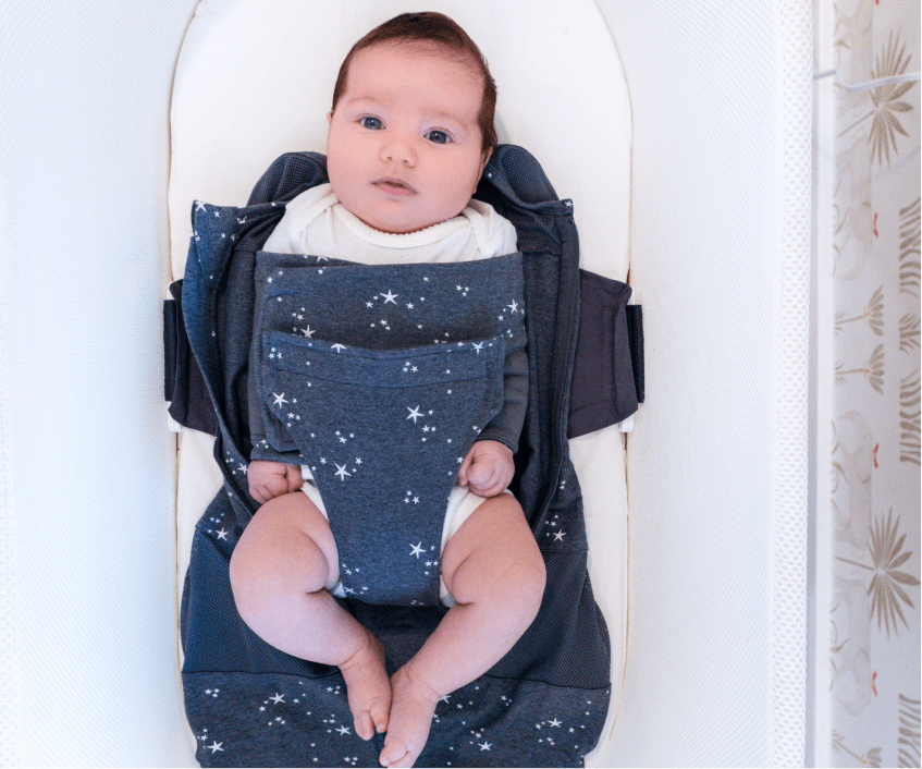 A baby in the SNOO bassinet while the mother wraps them in a swaddle